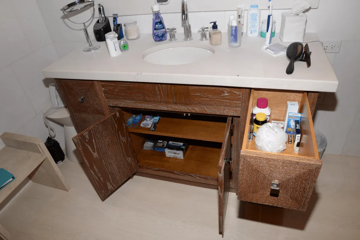 Wooden bathroom vanity with open doors and drawers showing interior shelving in a California home
